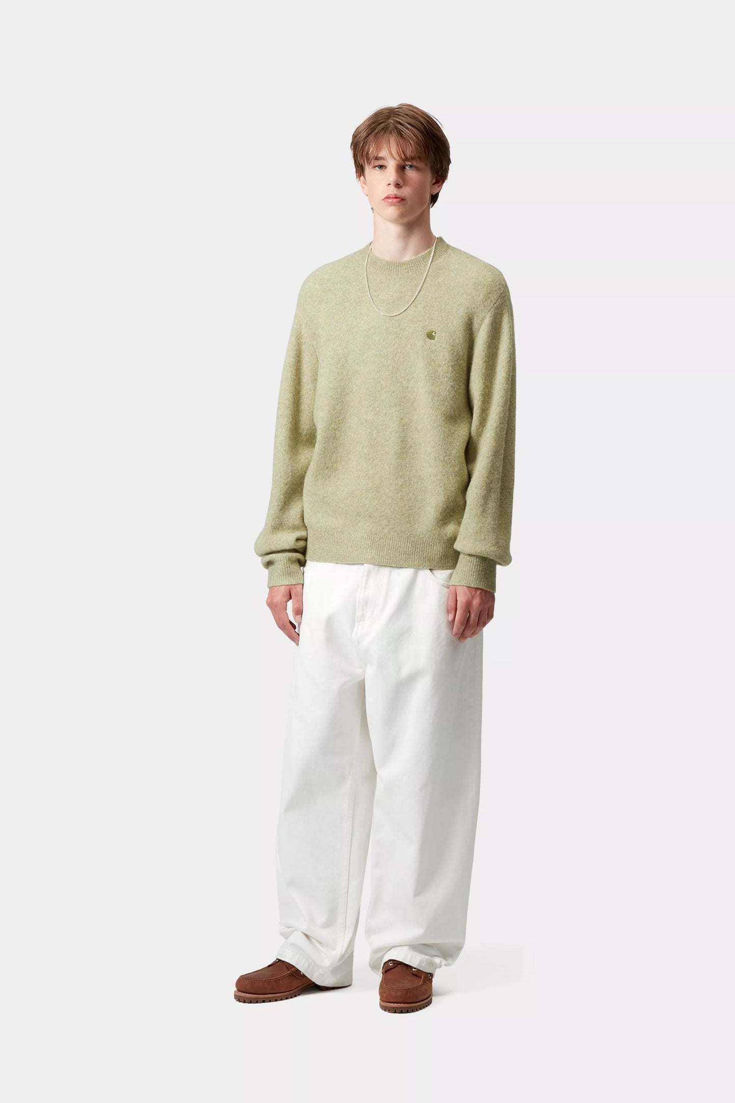 Person wearing a green sweater and white pants on a white background