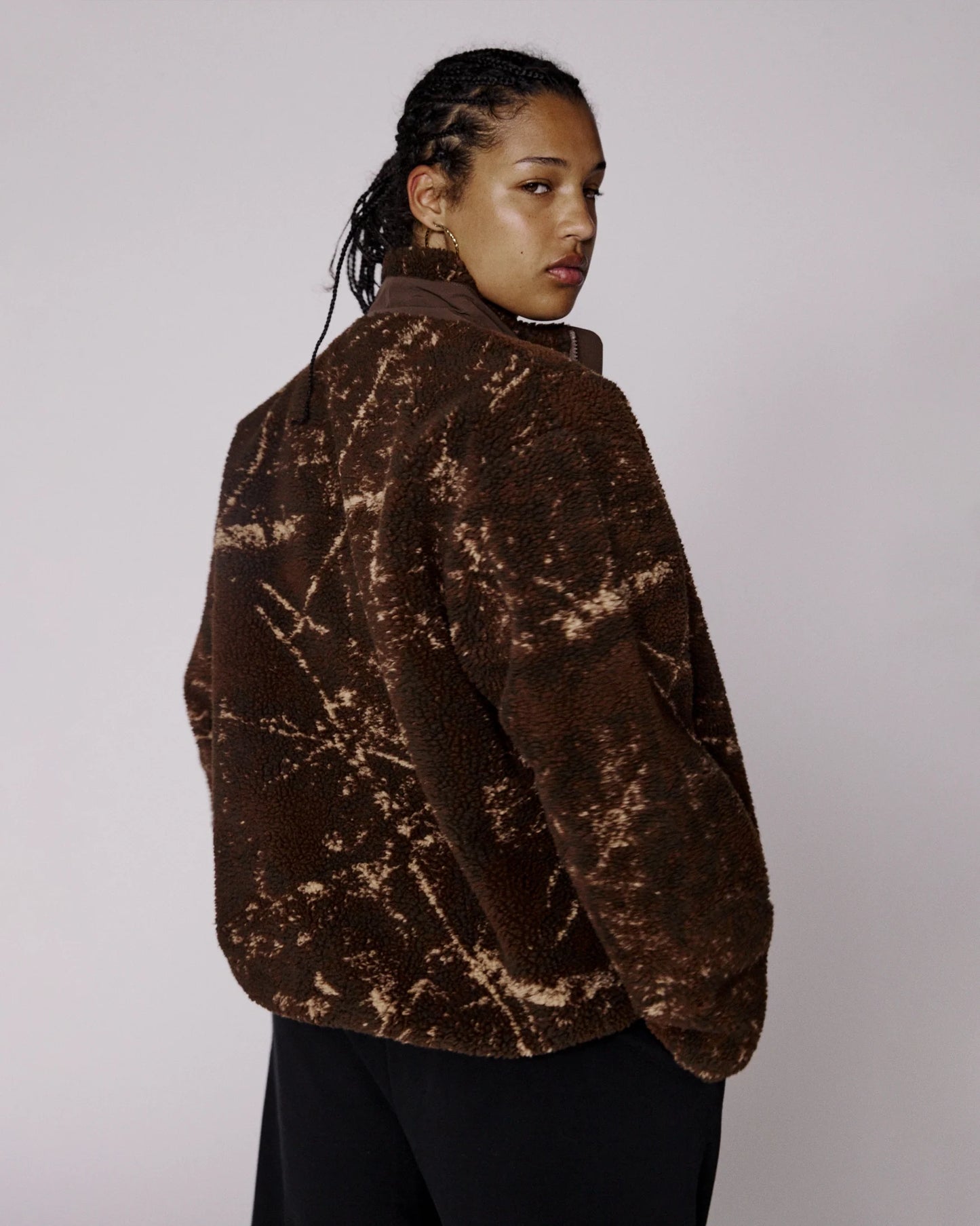 Person wearing a brown tie-dye jacket on a plain background