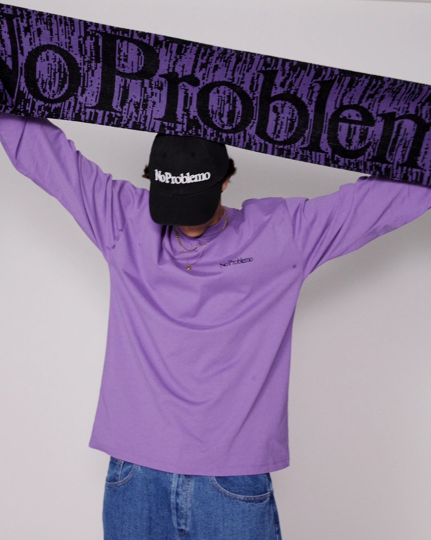 Person wearing a purple long-sleeve shirt and black cap with 'No Problem' text, holding a purple bandana.