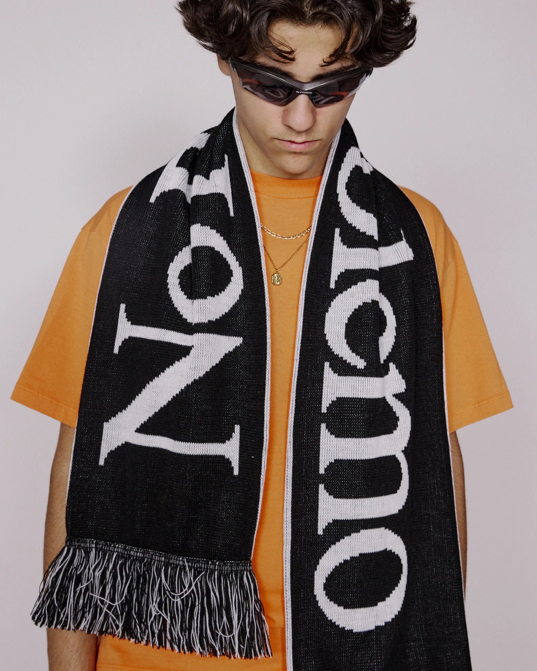 Person wearing a black scarf with white text over an orange shirt on a plain background
