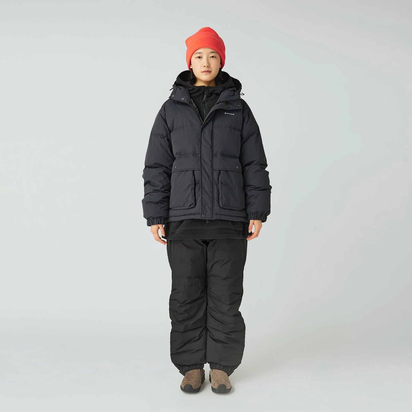 Person wearing a black winter jacket and pants with a red beanie on a white background