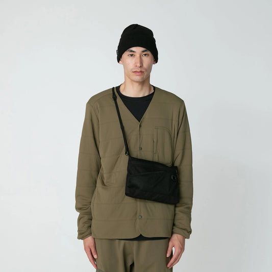 Person wearing a green jacket and black beanie with a black bag over one shoulder on a white background