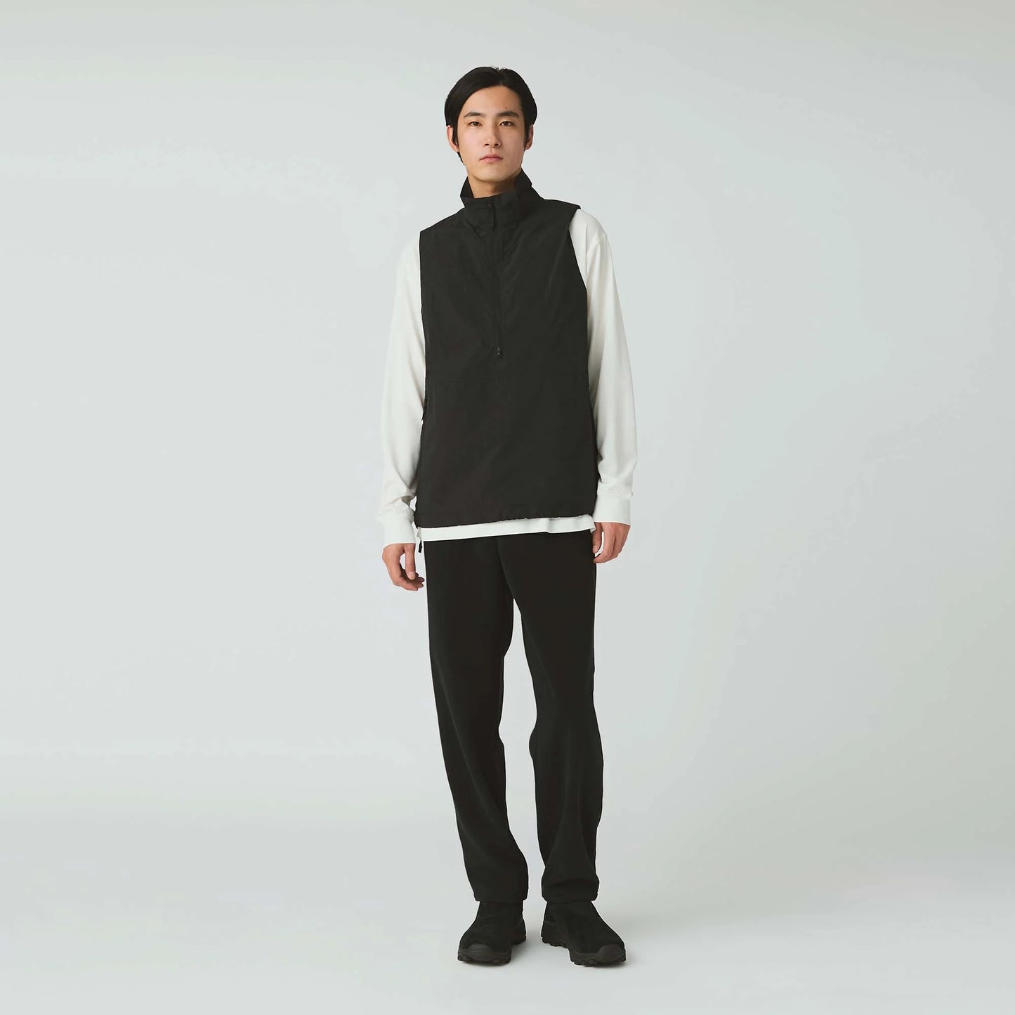 Person wearing a black vest over a white shirt with black pants on a white background