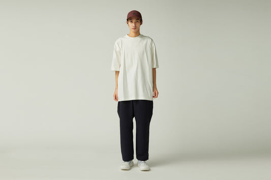 Person wearing a white oversized t-shirt, black pants, and a maroon cap on a plain background