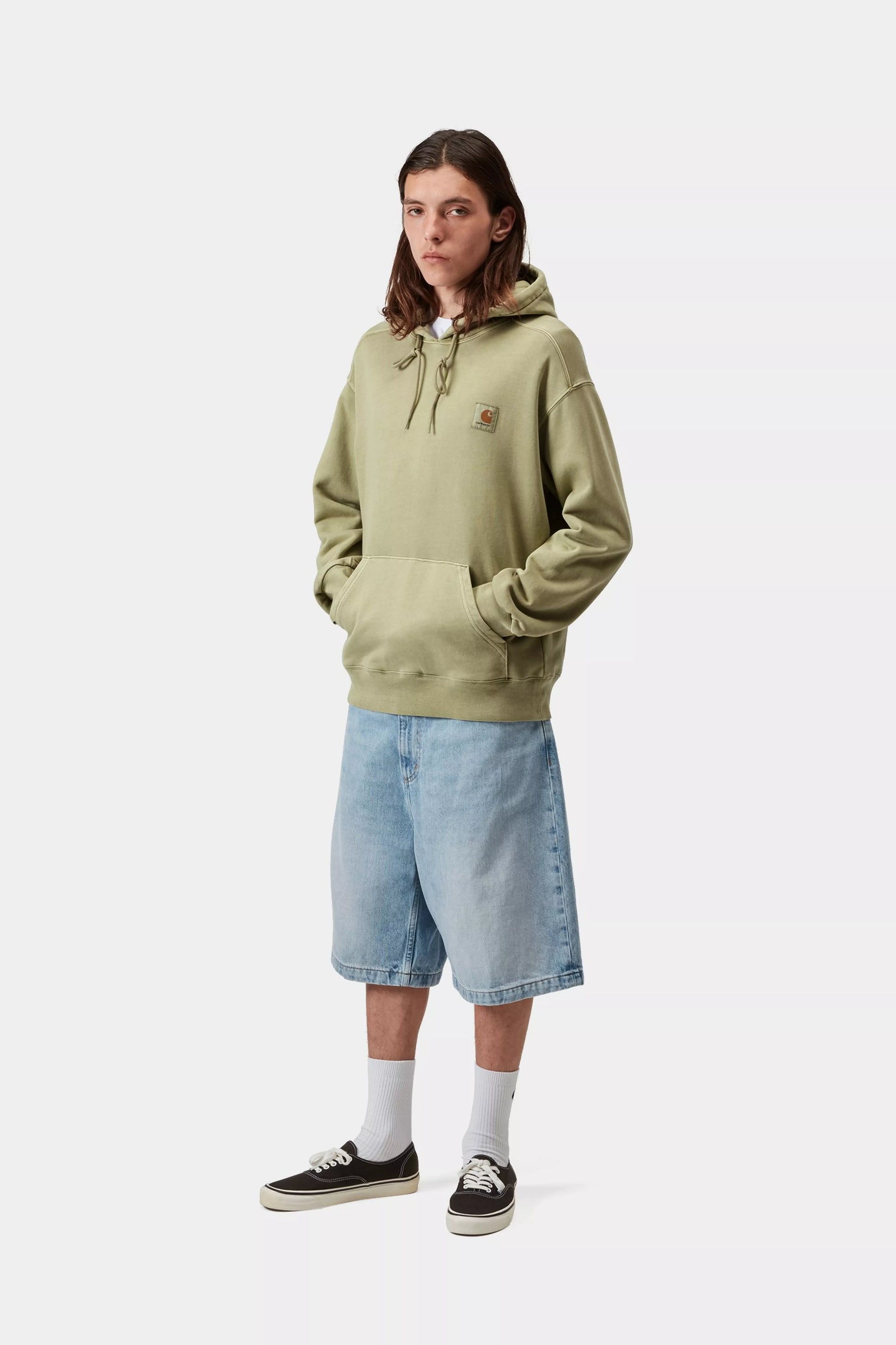 Person wearing a light green hoodie and denim shorts on a white background