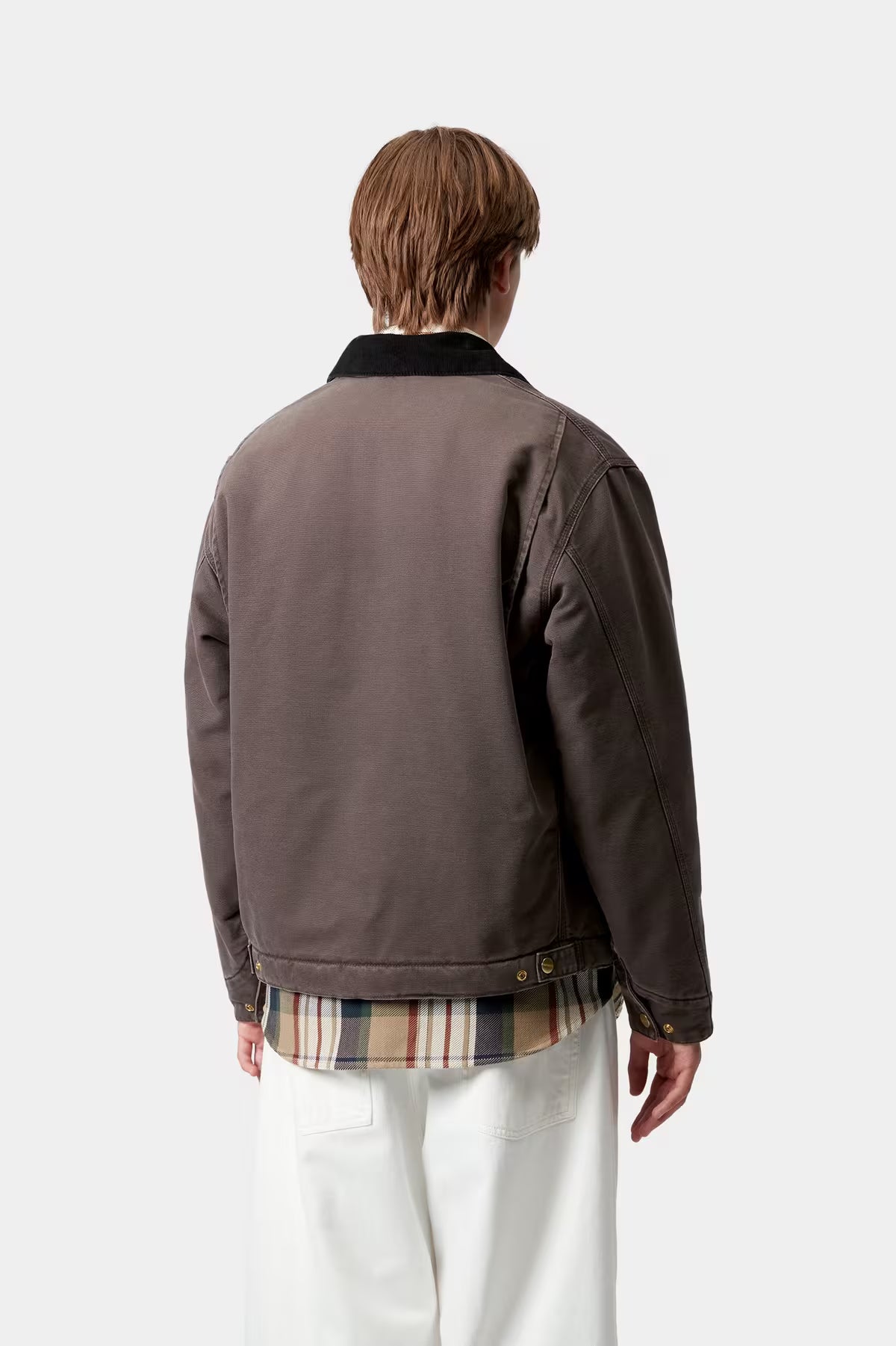 Person wearing a brown jacket with a plaid shirt and white pants on a white background
