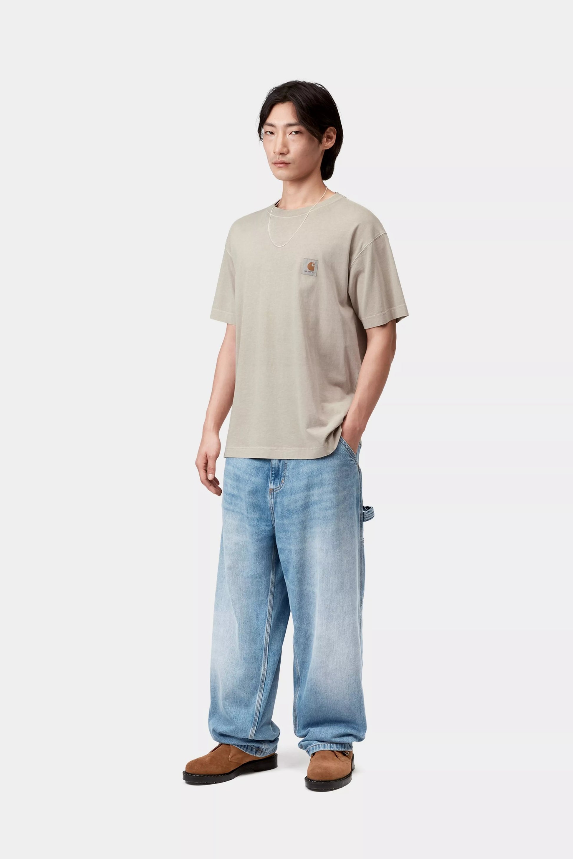 Person wearing a beige t-shirt and light blue jeans on a white background