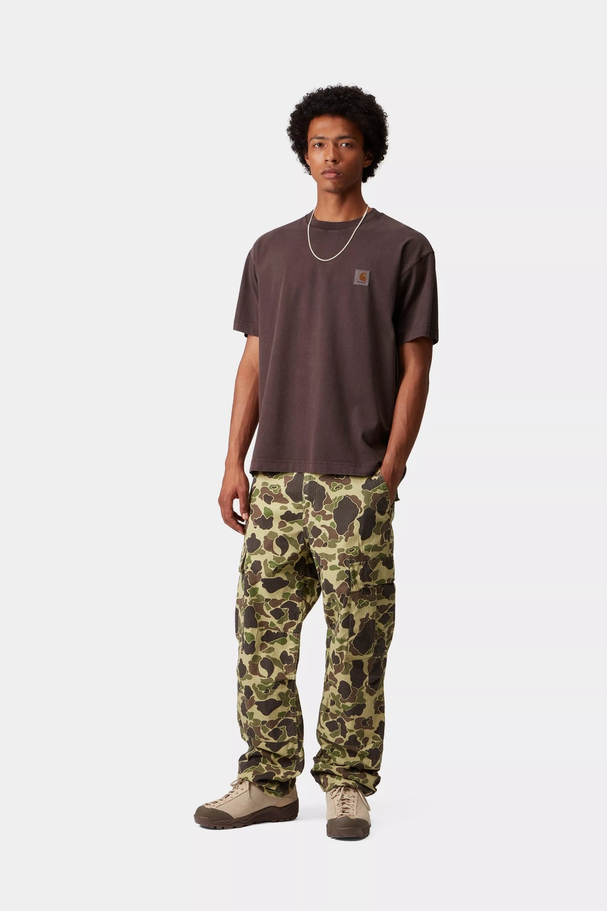 Person wearing a brown t-shirt and camouflage pants on a white background