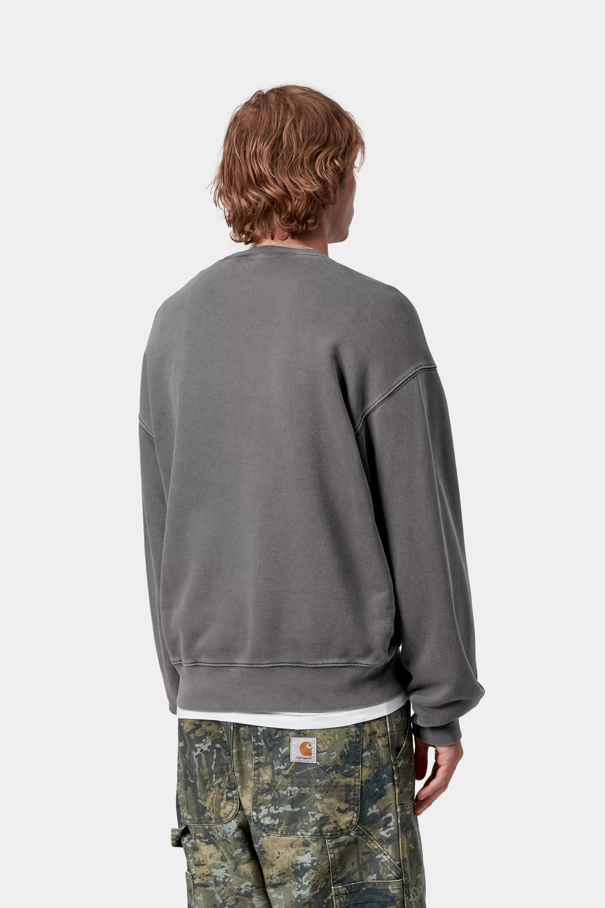 Person wearing a gray sweatshirt and camouflage pants on a white background