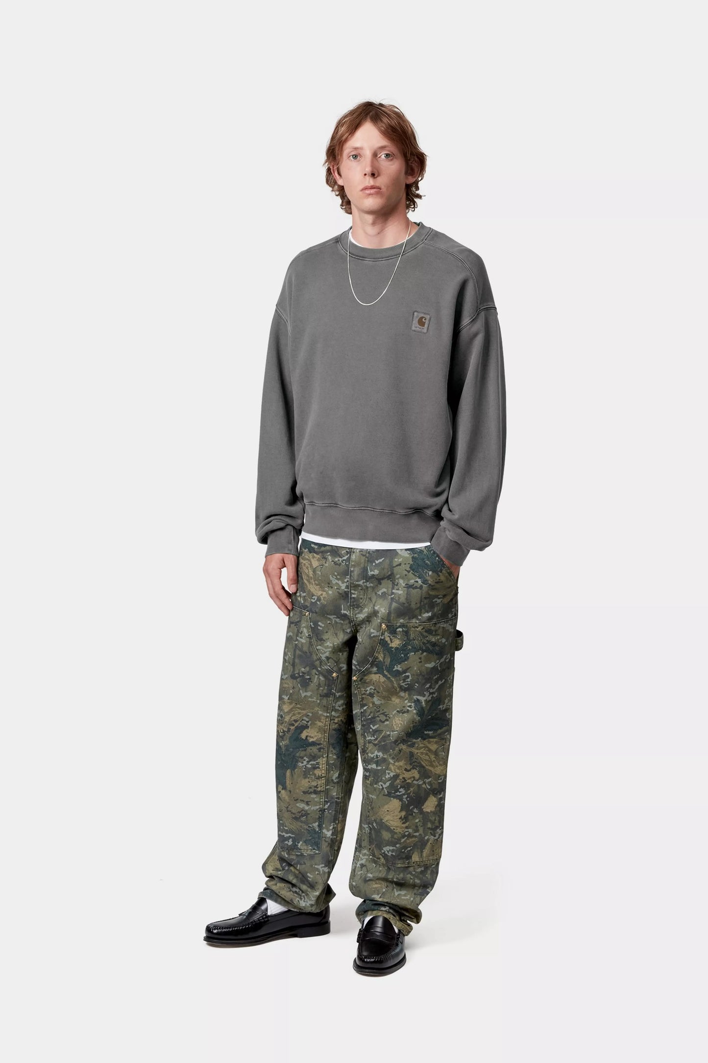 Person wearing a gray sweatshirt and camouflage pants on a white background