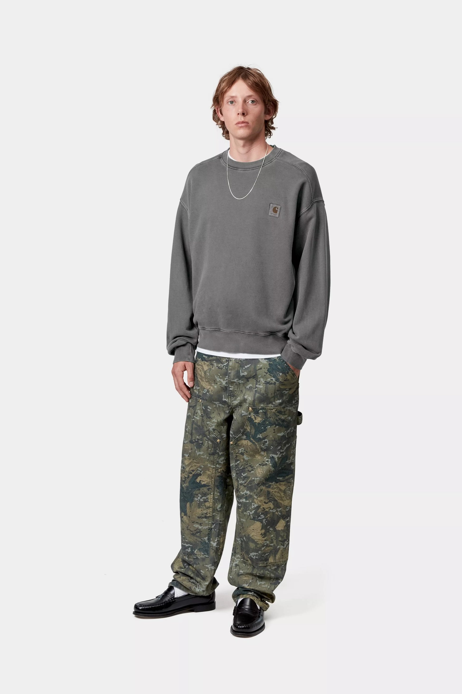 Person wearing a gray sweatshirt and camouflage pants on a white background