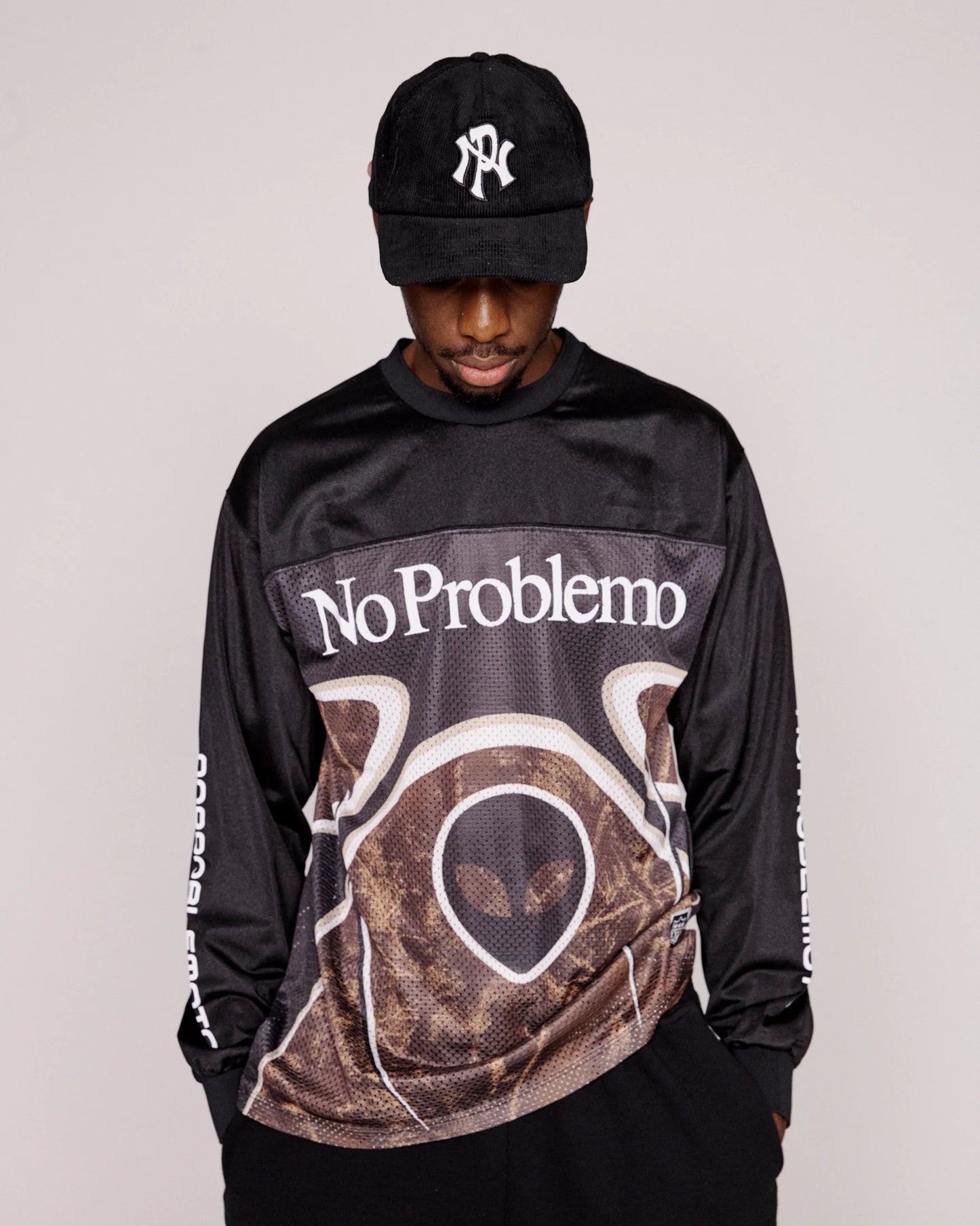 Person wearing a black long-sleeve shirt with 'No Problemo' text and a cap on a plain background