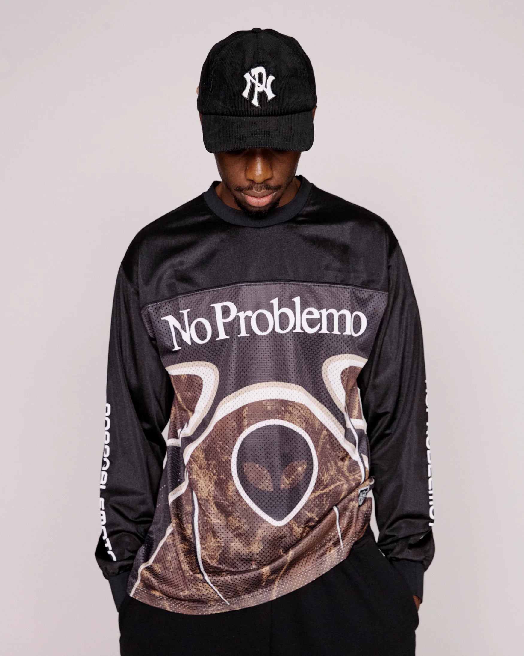 Person wearing a black long-sleeve shirt with 'No Problemo' text and a cap on a plain background