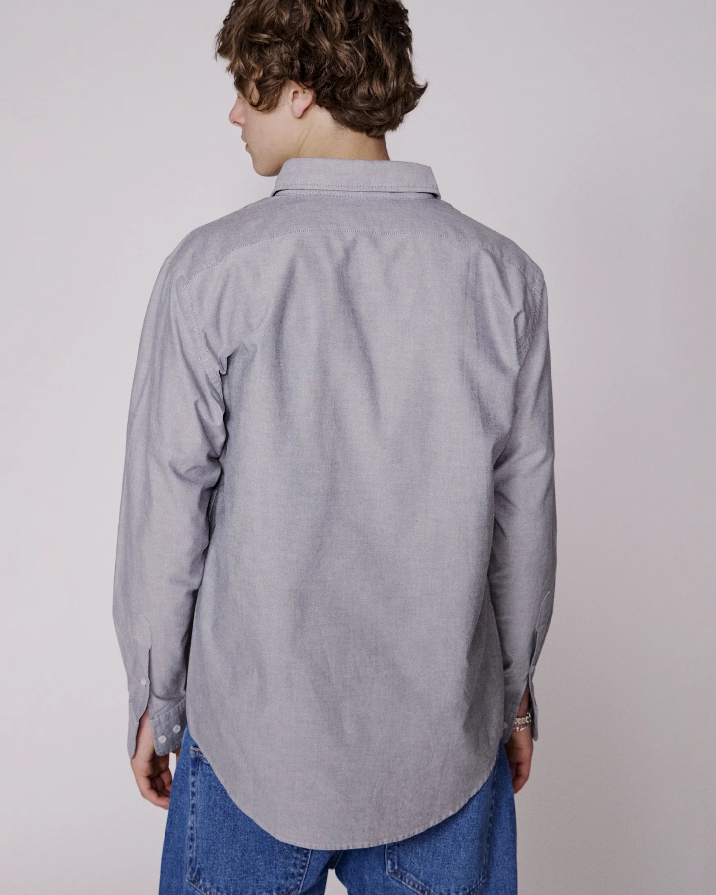 Person wearing a gray button-up shirt and blue jeans on a plain background