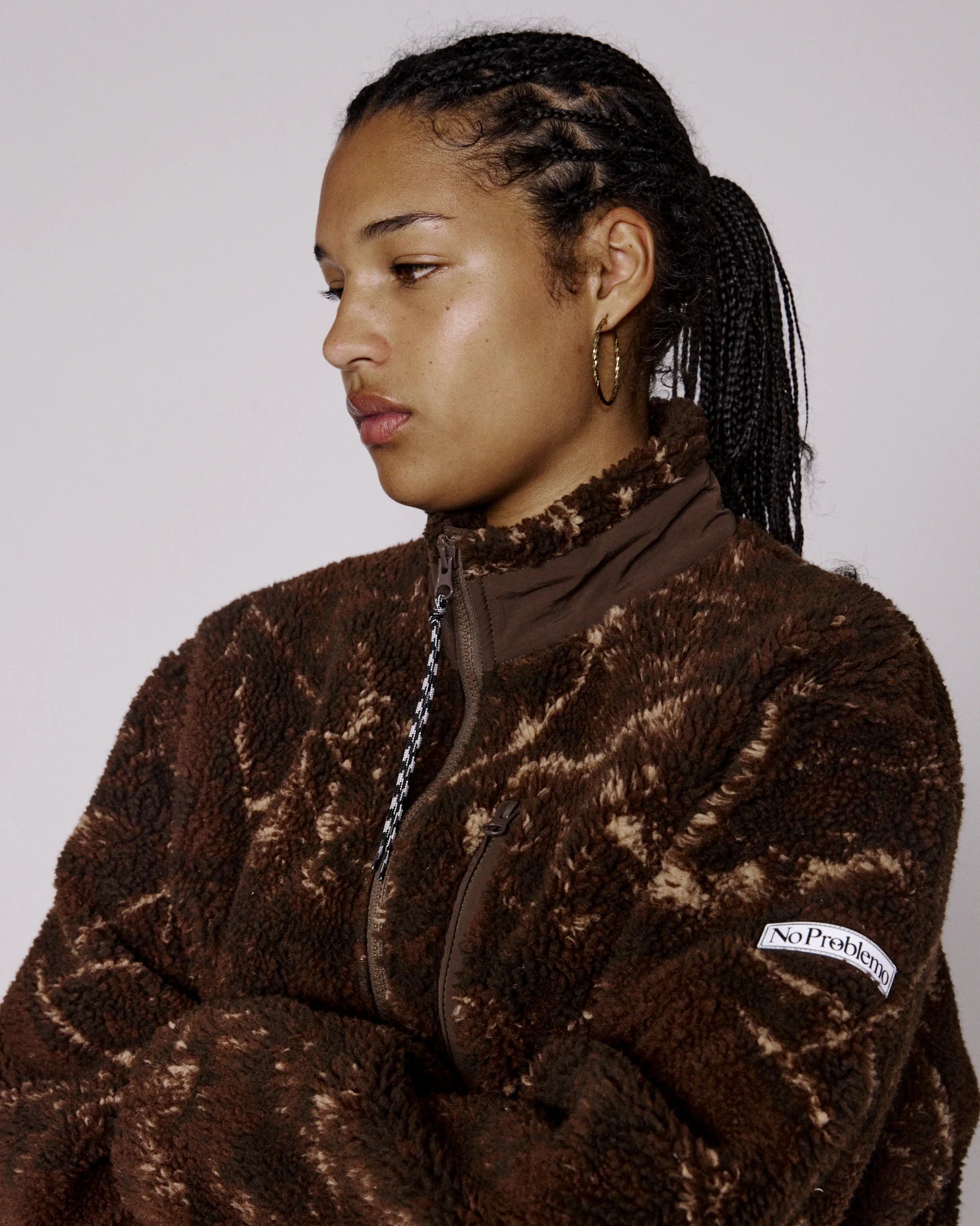 Person wearing a brown patterned jacket with a visible brand logo on a plain background
