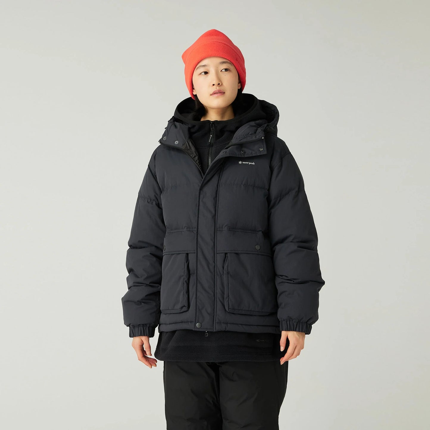 Person wearing a black jacket and red beanie on a light gray background