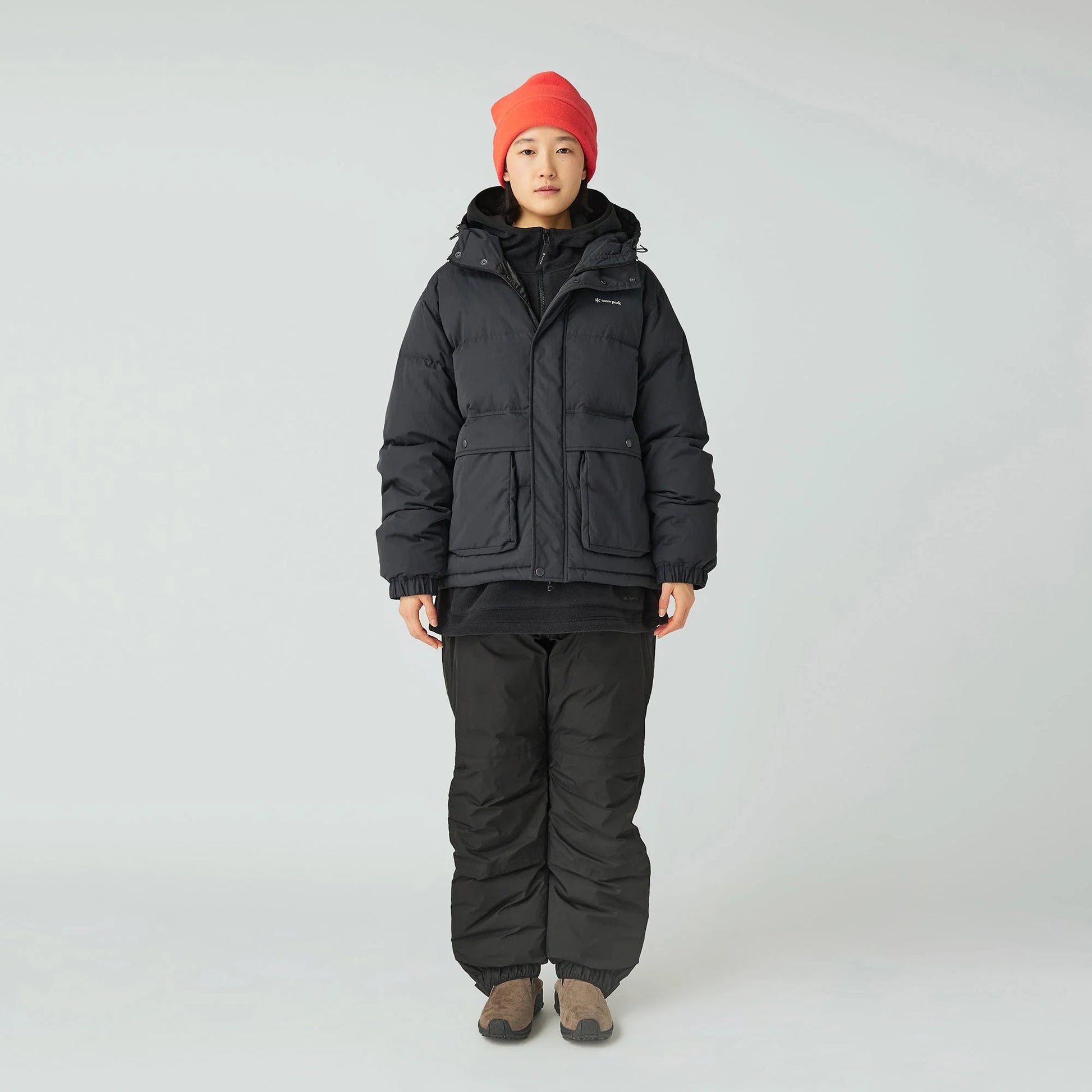 Person wearing a black winter jacket and pants with a red beanie on a white background