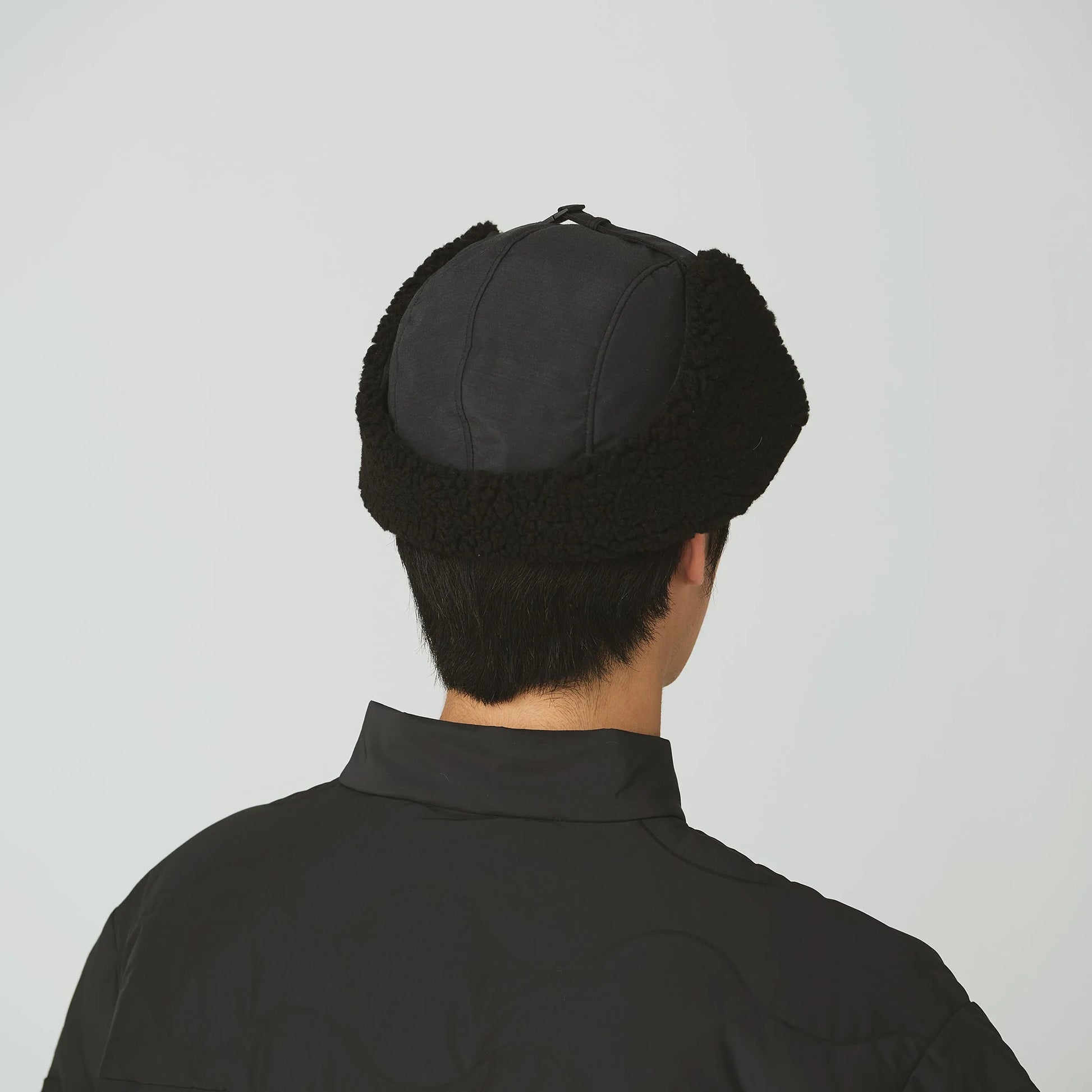 Person wearing a black fur-lined hat on a plain background