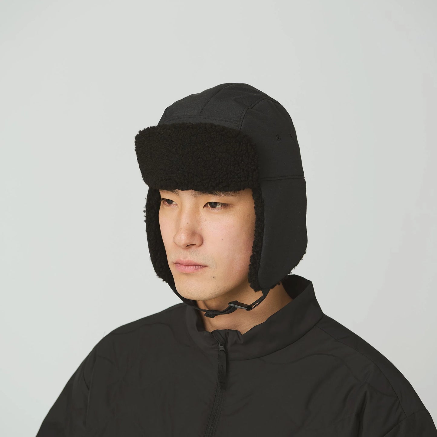 Person wearing a black winter hat with ear flaps on a light gray background