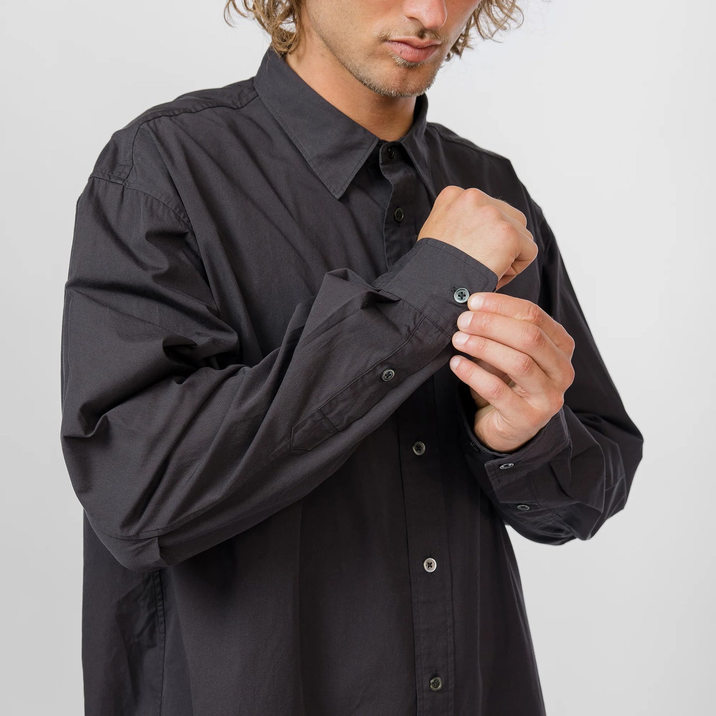 Man adjusting the sleeve of a black shirt against a plain background