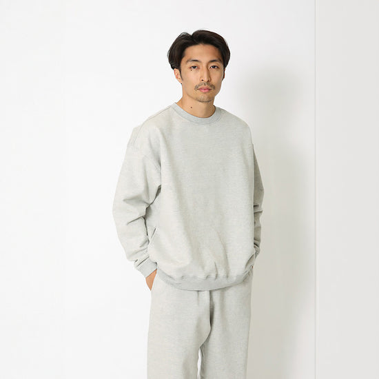 Man wearing a light gray sweatshirt and pants against a white background