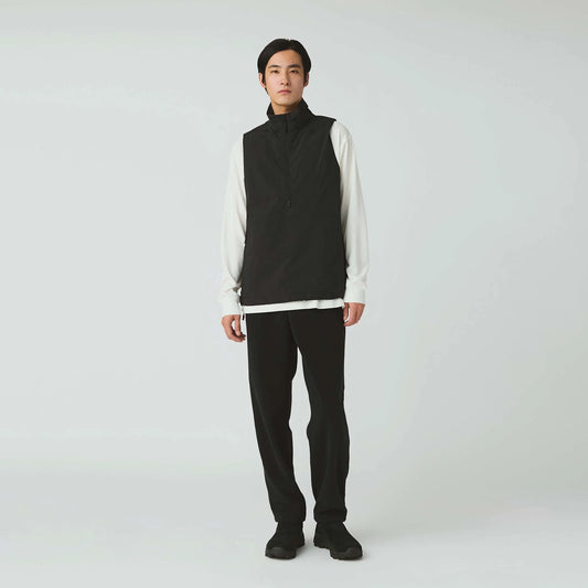 Person wearing a black vest over a white shirt with black pants on a white background