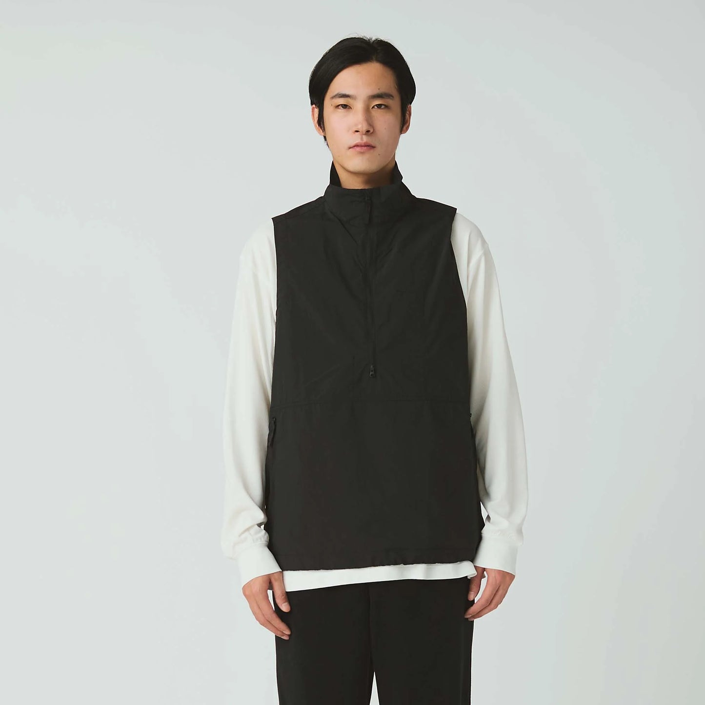Person wearing a black vest over a white shirt on a plain background