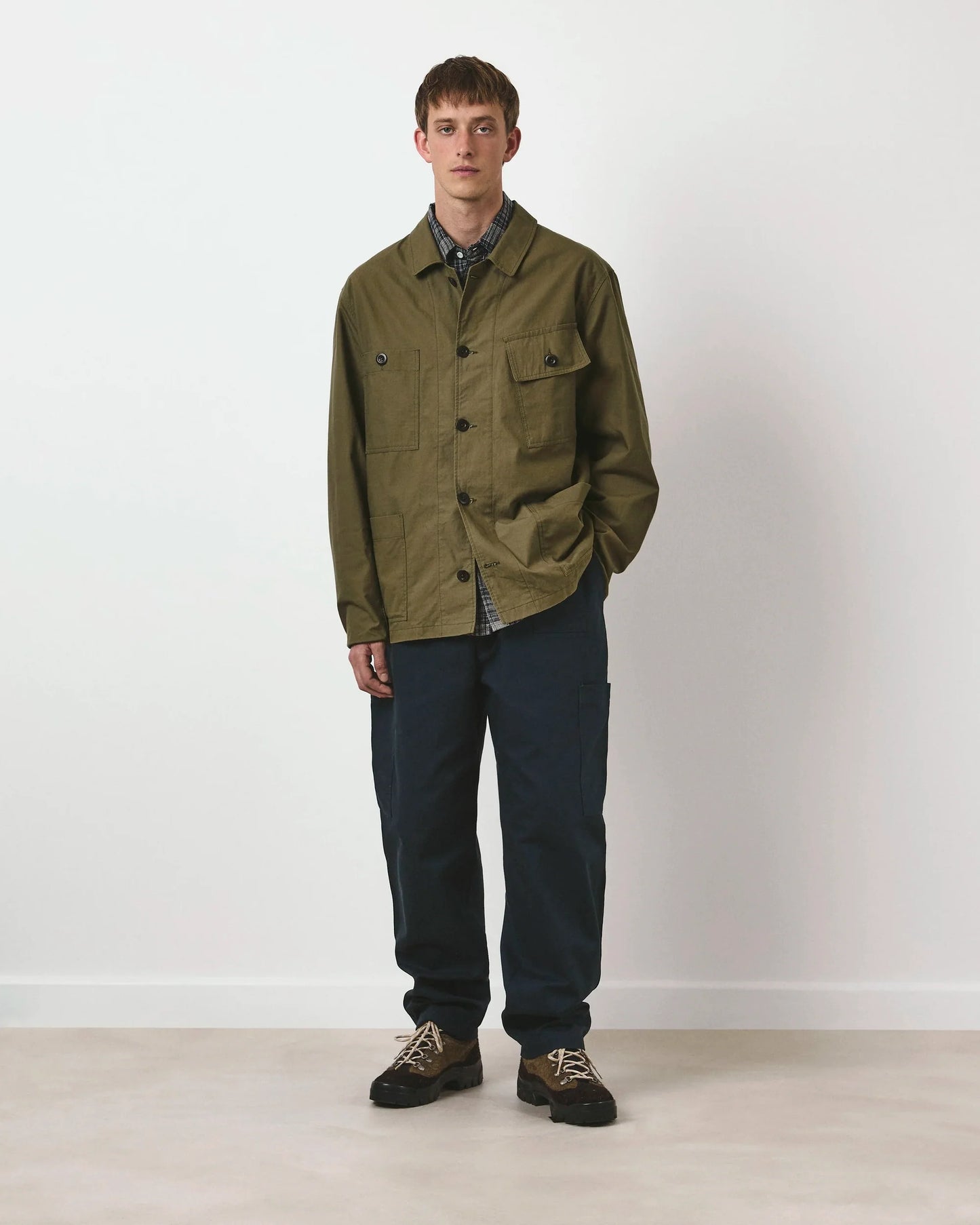 Man wearing an olive green jacket and dark pants against a white background