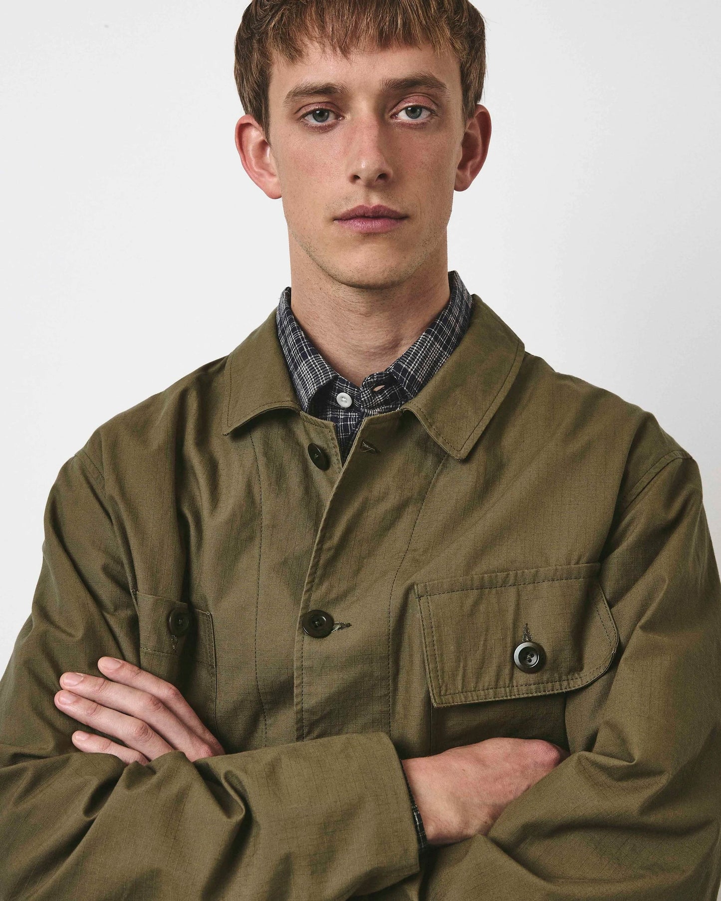 Man wearing a green jacket over a plaid shirt on a plain background